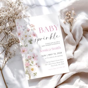 Peut inclure: Une invitation à une baby shower avec les mots "BABY sprinkle" en rose et noir. L'invitation présente des illustrations florales à l'aquarelle en rose, blanc et vert. Les détails incluent la date, l'heure et le lieu.