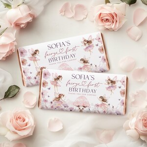 Puede incluir: Dos envoltorios de barras de chocolate con tem&aacute;tica de hadas. Los envoltorios presentan ilustraciones de hadas, flores y mariposas, con el texto "SOFIA'S fairye first BIRTHDAY THANK YOU FOR COMING!". Rodeado de rosas y p&eacute;talos rosas.