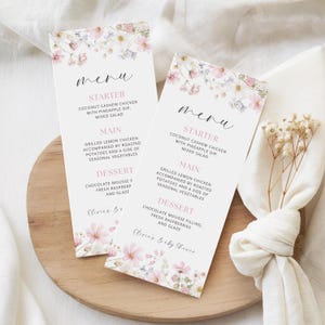 May include: Two vertical menu cards featuring a delicate watercolor floral border in shades of pink, white, and soft blue. The text includes "menu," "STARTER," "MAIN," "DESSERT," and "Olivia's Baby Shower" printed in black and pink ink.