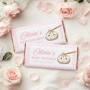 May include: Two chocolate bars with pink gingham wrappers and labels that read "Olivia's Baby Shower". Each bar features a cartoon dumpling with chopsticks. The background includes pink roses and petals.
