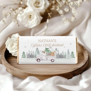 May include: A white chocolate bar with the text "NATHAN'S Winter ONEderland" in gold script. The bar features a watercolor illustration of a white truck carrying woodland animals and a Christmas tree, set against a snowy forest backdrop.