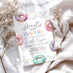 Może przedstawiać: Zaproszenie na baby shower z akwarelowymi pączkami i kolorową posypką. Tekst brzmi "Donuts and Diapers" ze szczegółami wydarzenia, w tym imieniem honorowanej osoby, datą, godziną i informacjami RSVP. Zaproszenie ma miękką, pastelową paletę kolorów.