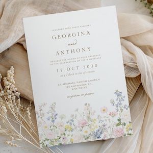 May include: A white rectangular wedding invitation card featuring dark brown serif text and a colourful watercolour floral border at the bottom. The text reads: Together with their families, Georgina and Anthony, request the honour of your presence at the celebration of their marriage, 17 Oct 2030, at 4 o'clock in the afternoon, St. Michael Parish Church, 123 Anywhere St., Any Drive, reception to follow.