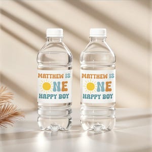 May include: Two clear plastic water bottles with white caps. Each bottle has a label that reads "MATTHEW IS ONE HAPPY BOY" with a sun graphic. The labels are in orange, blue, and yellow.