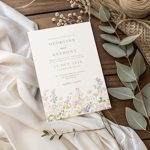 May include: A rectangular wedding invitation card with cream-coloured paper featuring a floral illustration at the bottom. The text reads: Together with their families, Georgina and Anthony, request the honour of your presence, 17 Oct 2030.