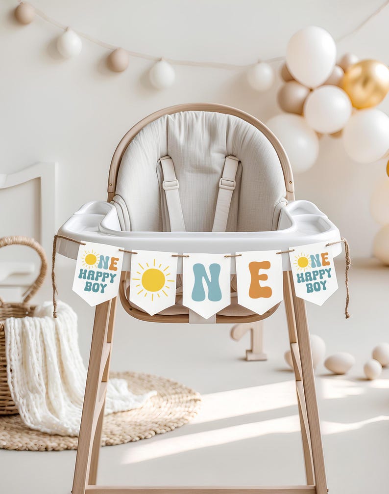 May include: A wooden high chair with a beige seat and a banner that reads "ONE HAPPY BOY." The banner has a yellow sun graphic and is strung across the front of the chair. Balloons in white and gold are in the background.