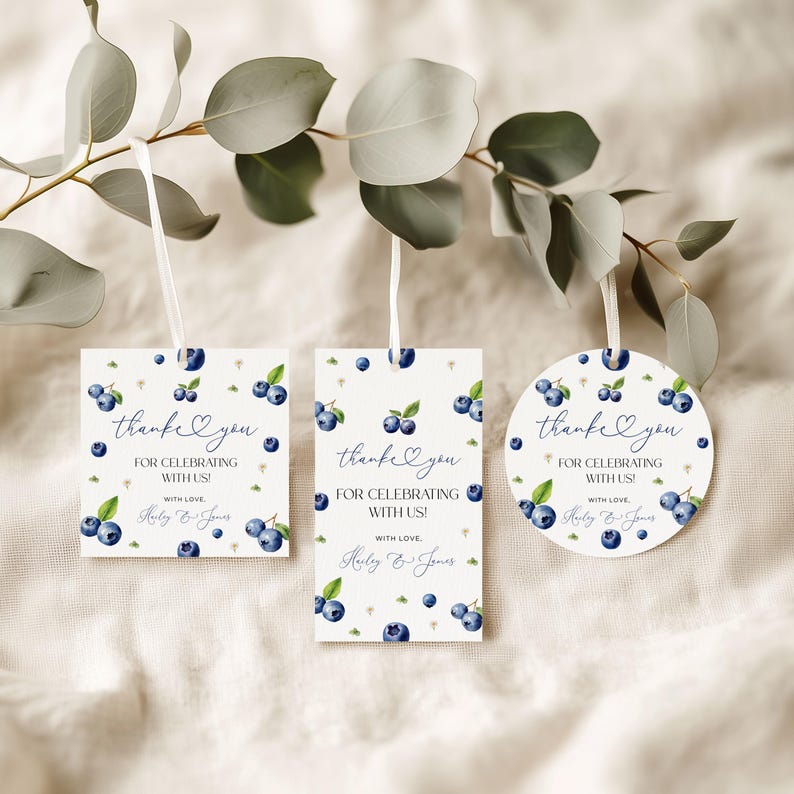 May include: Three gift tags with a blueberry design. The tags are square, rectangular, and circular, each with a white ribbon. Text on the tags reads "thank you for celebrating with us!" and a name.