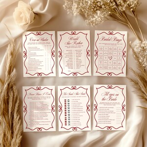 May include: Six ivory-colored bridal shower game cards with burgundy decorative borders and text. Games include "Over or Under," "Would She Rather," "Bridal Bingo," "Never Have I Ever," "She Said, She Said," and "All Eyes on the Bride."
