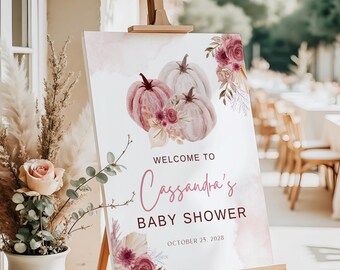 May include: A baby shower welcome sign on an easel. The sign features watercolor pumpkins in shades of pink and white, with floral accents. Text reads "Welcome to Cassandra's Baby Shower, October 25, 2028."