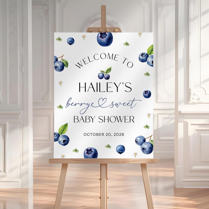 May include: A white baby shower welcome sign on a wooden easel. The sign features watercolor blueberries, leaves, and flowers. Text reads "Welcome to Hailey's berry sweet Baby Shower" with the date October 20, 2028.