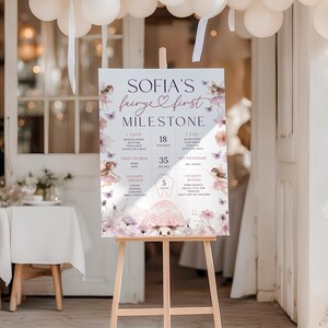Puede incluir: Un caballete de madera exhibe un letrero de hito para "Sofia's Fairye First Milestone". El letrero presenta un tema de hadas con detalles florales y mariposas, e incluye detalles como "8 kg" y "89 cm."
