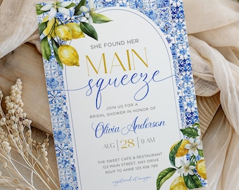 May include: Bridal shower invitation with a blue and white tile pattern. The invitation has the text "She Found Her Main Squeeze" in gold and blue script, with lemon and floral accents. The date and time are also included.