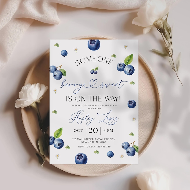 May include: A white invitation card with a blueberry theme. The text reads "Someone berry sweet is on the way!" with the name "Hailey Lopez" and event details. The card is decorated with blueberry illustrations.