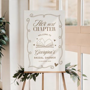 May include: A cream-colored sign on a wooden easel with the text "Her next CHAPTER welcome to Georgina's BRIDAL SHOWER 12 November 2030" in brown script. The sign has decorative swirls and a book illustration.