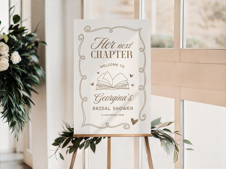 May include: A cream-colored sign on a wooden easel with the text "Her next CHAPTER welcome to Georgina's BRIDAL SHOWER 12 November 2030" in brown script. The sign has decorative swirls and a book illustration.