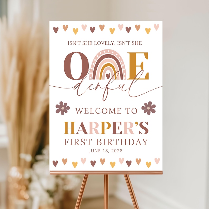 Peut inclure: Panneau blanc sur un chevalet en cuivre avec le texte "Isn't she lovely, isn't she" au-dessus du mot "One" avec un motif arc-en-ciel. Le panneau indique "Welcome to Harper's First Birthday, June 18, 2028" avec des c&oelig;urs et des fleurs.