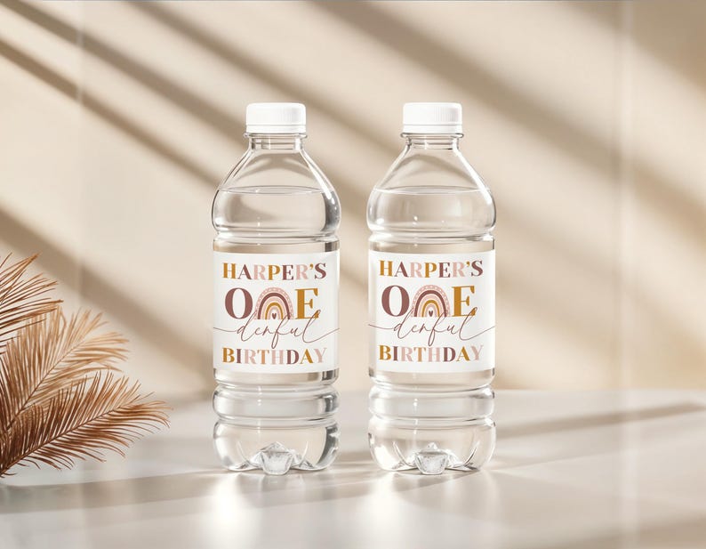 Peut inclure: Deux bouteilles d'eau en plastique transparent avec des bouchons blancs. Chaque bouteille porte une &eacute;tiquette avec le texte "HARPER'S ONE derful BIRTHDAY" et un arc-en-ciel marron et dor&eacute;. Les bouteilles sont sur une surface claire.