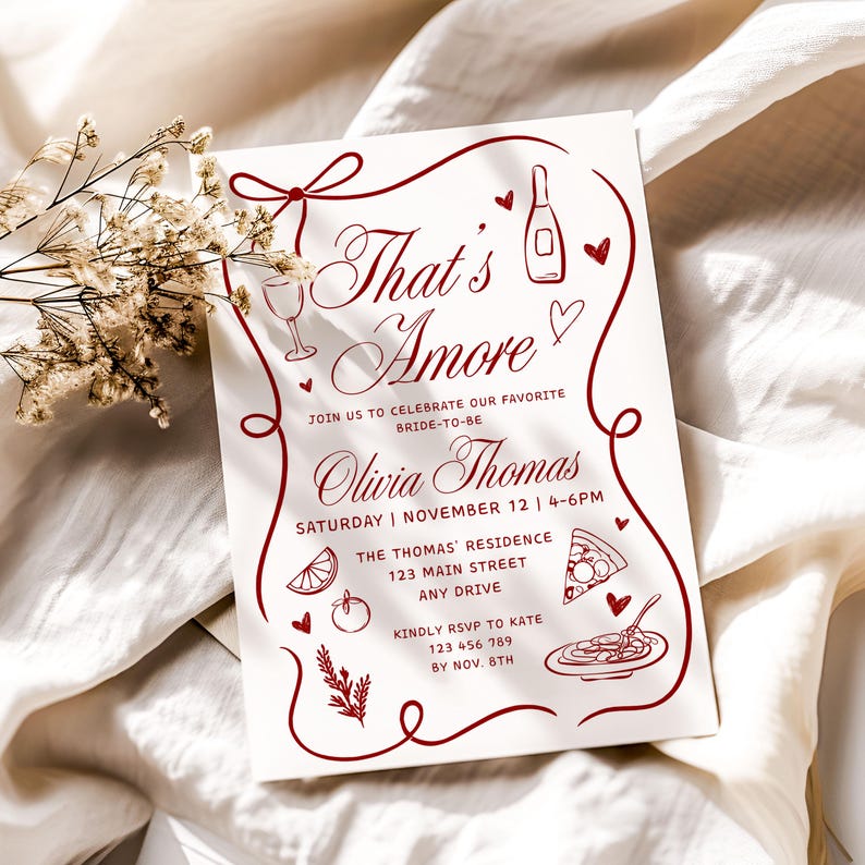 May include: A white invitation card with burgundy text and illustrations. The text reads "That's Amore" and includes details for a bridal shower, such as the date, time, and location. Decorative elements include hearts, a wine bottle, and food illustrations.