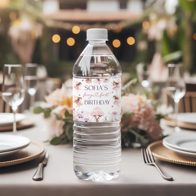 Puede incluir: Una botella de agua de pl&aacute;stico transparente con tapa blanca. La etiqueta dice "SOFIA'S fairy & first BIRTHDAY" con ilustraciones de hadas y setas en rosa y morado. La botella est&aacute; sobre una mesa puesta para una fiesta.