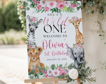 Op de afbeelding: Een houten ezel toont een bord voor Olivia's 1e verjaardag. Het bord toont een zebra, giraf, leeuw en olifant, elk met een bloemenkrans. De tekst luidt "She's a Wild One" en "Welcome to Olivia's 1st Birthday, January 25, 2028."