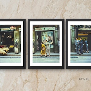 Puede incluir: Conjunto de tres impresiones enmarcadas que presentan escenas callejeras vintage. Las imágenes muestran personas y tiendas en un entorno de Oriente Medio, con una paleta de colores cálidos y una estética retro. Los marcos son negros y el estilo recuerda a la fotografía de viajes.