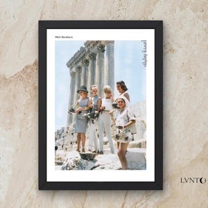 May include: Framed print featuring a vintage photograph of a group of people posing in front of ancient columns. The image is in color, with the text "1963 | Baalbeck" at the top. The frame is black, and the background is a textured beige.