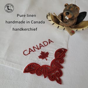 May include: White linen handkerchief with red embroidered "CANADA" text and maple leaf. Features a decorative red lace corner. The text "Pure linen handmade in Canada handkerchief" is also visible.