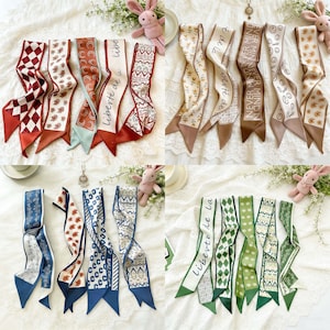 Puede incluir: Una variedad de pañuelos de seda con diversos patrones y colores, incluyendo diseños florales, geométricos y con texto. Algunos pañuelos presentan las frases "Liberté de la" y "Never Mind". Los pañuelos están dispuestos sobre una superficie blanca texturizada.