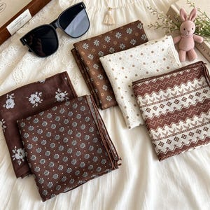 May include: An assortment of folded brown and white patterned handkerchiefs. Designs include floral, polka dot, and geometric patterns. Black sunglasses and a small stuffed bunny are also visible.