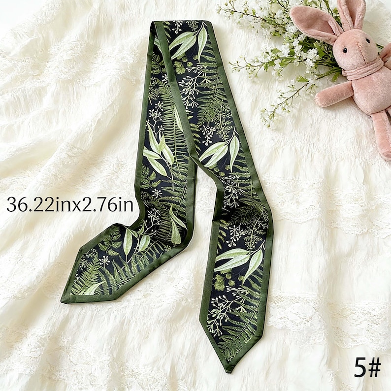 May include: A dark green scarf with a botanical pattern featuring leaves and ferns. The scarf measures 36.22 inches long and 2.76 inches wide. The scarf is on a white lace surface. The number 5# is in the bottom right corner.