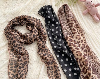 May include: Three long, rectangular scarves made of lightweight, semi-sheer fabric. One scarf features a brown and black leopard print, another has a black background with white polka dots, and the third displays a mixed leopard and animal print pattern.