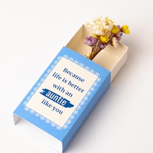May include: A blue and white matchbox-style gift box with the text "Because life is better with an auntie like you." The box contains a small bouquet of dried flowers in yellow, purple, and white.