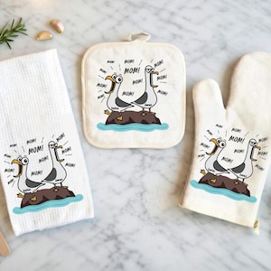 May include: A kitchen set featuring a white waffle-weave towel, a square pot holder, and an oven mitt. Each item displays a cartoon of two seagulls on a rock, with the word "MOM!" in speech bubbles. The set is designed for kitchen use.