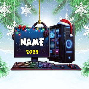 May include: A festive Christmas ornament featuring a gaming PC setup. The ornament includes a monitor with the name "NAME" and the year "2024", a keyboard, mouse, and a PC tower with a Santa hat. The background is a snowy scene with snowflakes.