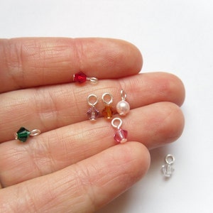 May include: Assortment of small, colorful crystal beads with silver jump rings. The beads are in shades of red, green, pink, orange, and white.