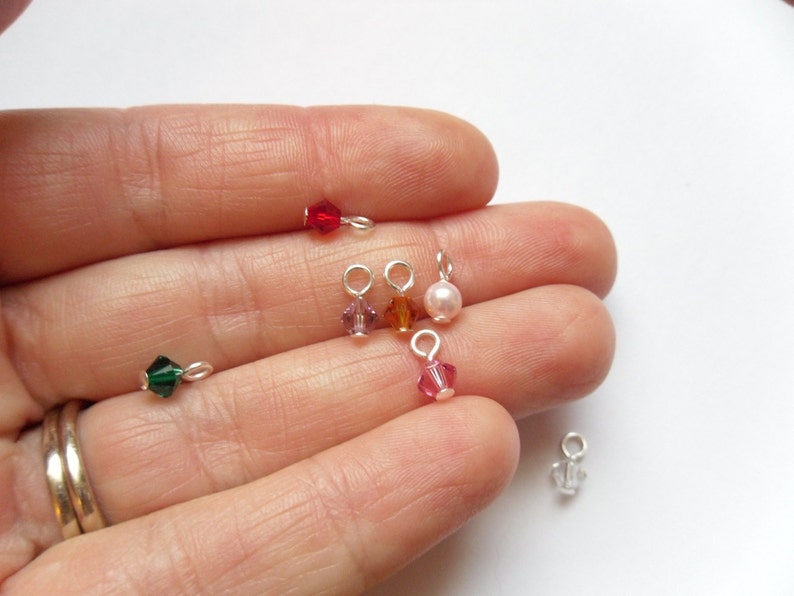 May include: Assortment of small, colorful crystal beads with silver jump rings. The beads are in shades of red, green, pink, orange, and white.