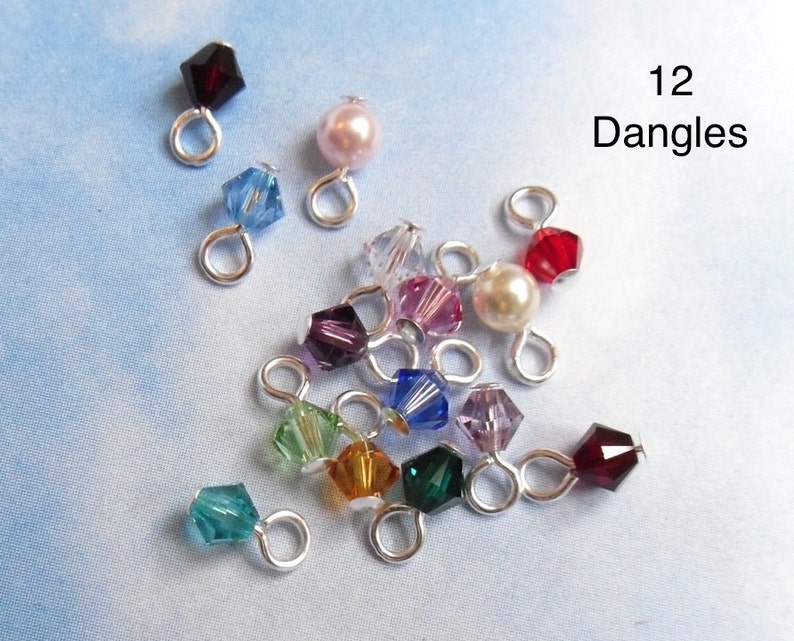 May include: Twelve assorted crystal and pearl dangles with silver loops. The dangles are in various colors, including red, blue, green, purple, and pink.