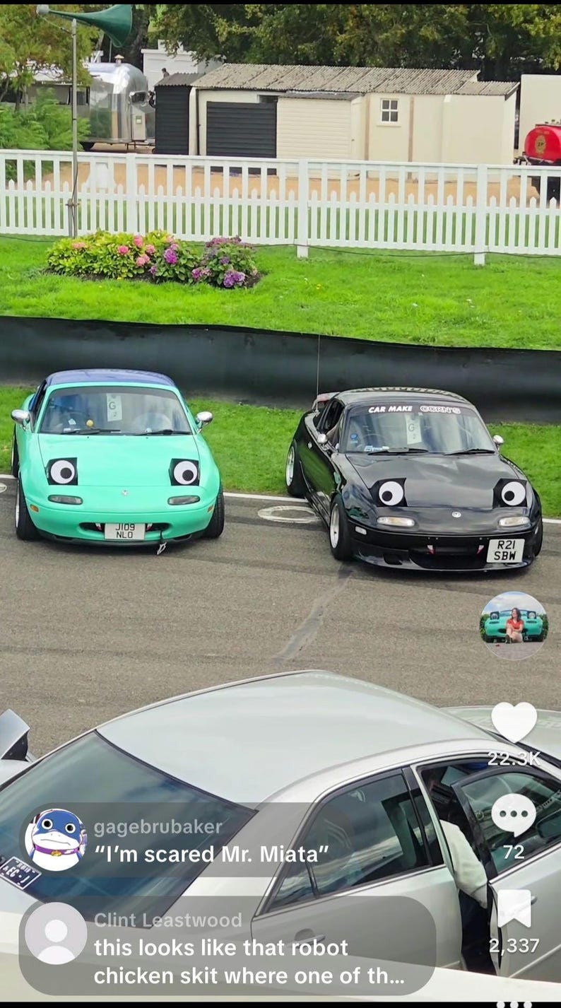 May include: Two Mazda Miata cars, one teal and one black, with cartoon-like eyes on the headlights. The teal car has a license plate that reads "JI09 NLO". The black car has a license plate that reads "R21 SBW".
