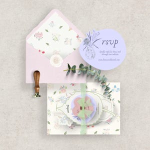 Peut inclure: Une enveloppe rose clair avec une doublure &agrave; motifs floraux, une carte RSVP ronde et une invitation d&eacute;corative avec un motif floral. Un tampon &agrave; cacheter &agrave; manche en bois et des brins de verdure compl&egrave;tent l'ensemble de papeterie.