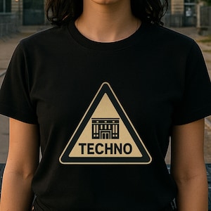 May include: Black t-shirt with a yellow and black triangular graphic that reads "TECHNO". The graphic features a building design. The person in the image is standing in front of a building.