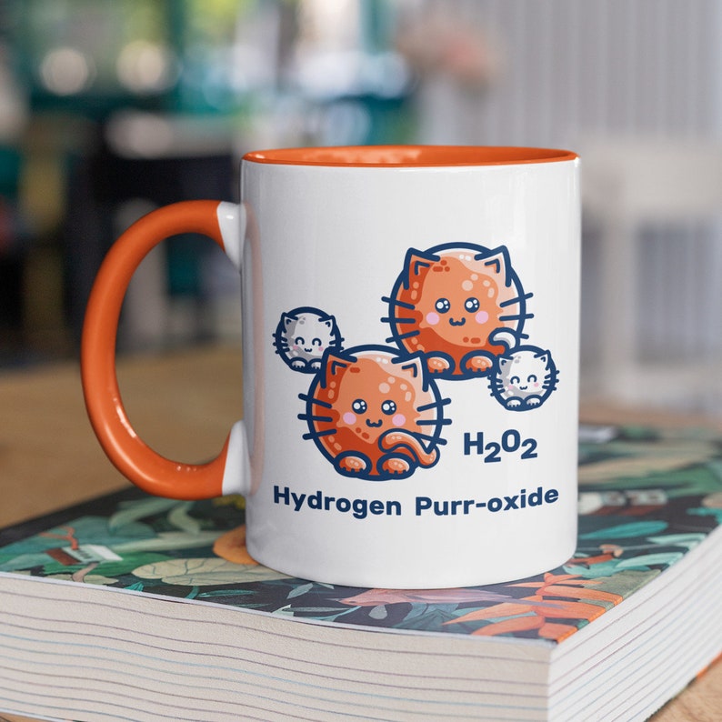K&ouml;nnte beinhalten: Wei&szlig;e Keramiktasse mit orangefarbenem Rand und Henkel. Die Tasse zeigt eine Cartoon-Illustration von orangefarbenen Katzen mit dem Text "H2O2 Hydrogen Purr-oxide".