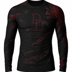 Puede incluir: Camiseta negra de manga larga con un patrón texturizado y detalles en rojo. La camiseta presenta un gran logotipo "DD" rojo en el pecho y marcas de rasguños rojos en la tela. La camiseta tiene cuello redondo.