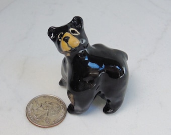 May include: A small black ceramic bear figurine with yellow painted eyes and nose. The bear is looking over its shoulder and has a glossy finish.
