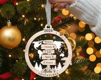 May include: A wooden Christmas ornament with a world map design and the year 2025. The ornament features destinations like Mexico, Canada, Italy, Spain, and France. The text "Alida's Adventures" is also included. The ornament is hanging on a Christmas tree.