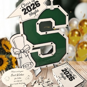 May include: A wooden graduation-themed display in the shape of the letter "S", with the text "Class of 2026 Shyla". Includes a mortarboard, diploma, and a box with the same text. A small sign reads "Please write your Best Wishes for Celine on a chip and drop it inside the frame."
