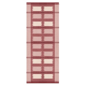May include: A rectangular rug with a geometric pattern in shades of red and cream. The design features alternating rectangular blocks and zig-zag shapes, with vertical stripes along the edges. The rug is likely made of woven material.