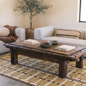 May include: A low rectangular coffee table crafted from dark, weathered wood with a thick, uneven plank top and four sturdy, cylindrical log legs. Two shallow, dark-toned bowls and two stacked books are placed on the surface of the wooden table.