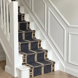 May include: A staircase featuring white steps and a navy blue stair runner with a geometric design. The runner has a beige border and a repeating pattern. White banisters and wall panelling provide a clean contrast to the runner's design.