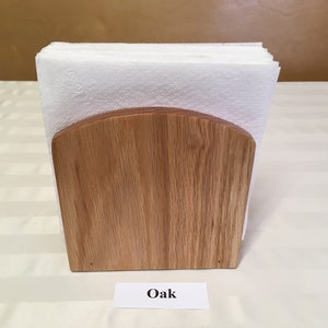 May include: A wooden napkin holder made of oak. The holder has a rounded top and is empty.