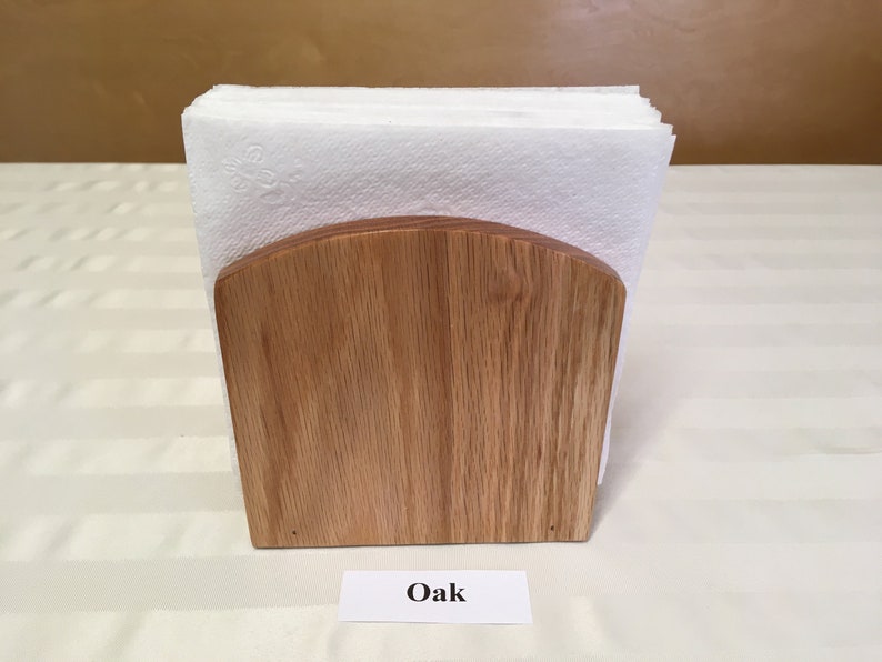 May include: A wooden napkin holder made of oak. The holder has a rounded top and is empty.